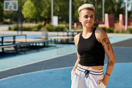 A young woman with short hair and tattoos stands on a basketball court, hands in pockets, exuding confidence and calmness.