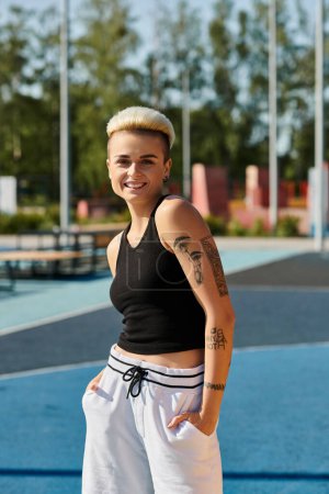 A young woman with short hair stands on a tennis court, showcasing a tattoo on her arm.