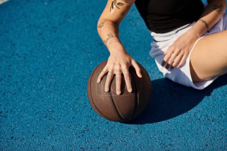 A young woman with tattoos sits on the ground holding a basketball, exuding an aura of determination and athleticism.