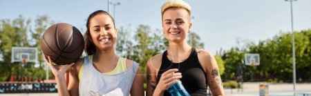 Deux jeunes femmes, athlétiques et en vêtements de sport, se tiennent ensemble à l'extérieur, tenant un ballon de basket.