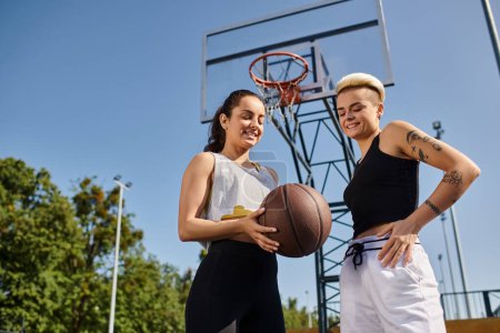 Two athletic young women dribbling a basketball outdoors on a sunny day, enjoying a friendly game together.