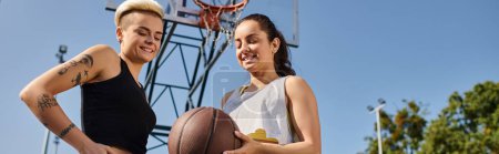 Zwei junge Frauen stehen zusammen, halten einen Basketball in der Hand und genießen an einem sonnigen Tag ein Spiel im Freien.
