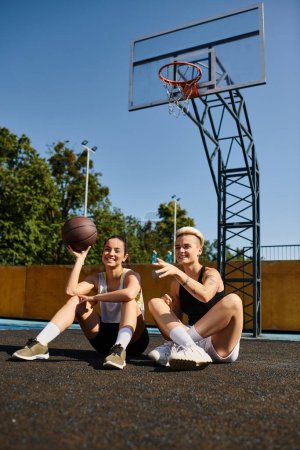 Two young women enjoy a game of basketball on the ground in the summer sun.