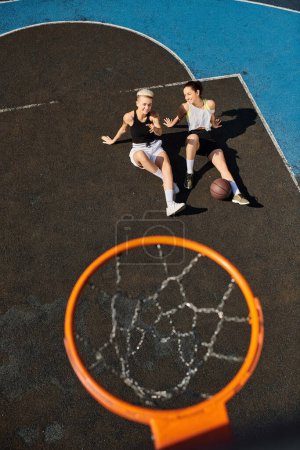 Zwei aktive junge Frauen genießen gemeinsam ein Basketballspiel auf einem sonnigen Außenplatz.
