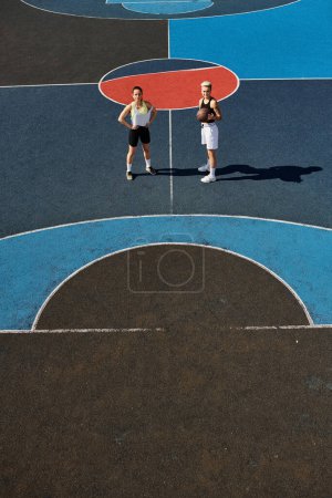 Dwie wysportowane młode kobiety stojące pewnie na boisku do koszykówki, gotowe do gry.