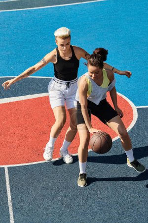 Two young women, friends and athletes, engaged in a competitive game of basketball on an outdoor court in the summer.