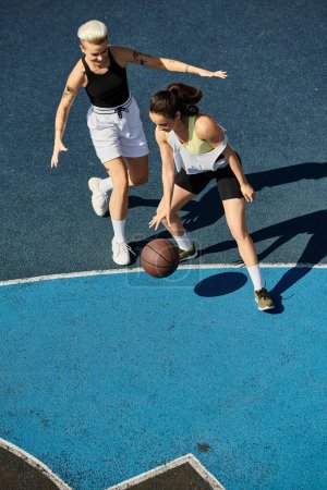 Two athletic female friends are immersed in a competitive game of basketball on an outdoor court during the summer.