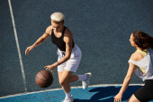 An intense game of basketball between two young women, friends showcasing their athletic skills on the outdoor court in summer. magic mug #705117640