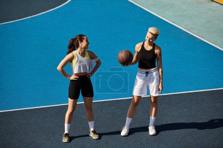 Dwie wysportowane młode kobiety, przyjaciele, stoją pewnie na boisku do koszykówki, ciesząc się letnim dniem.