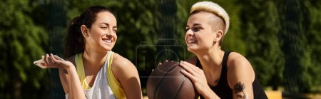 Zwei junge Frauen, Freundinnen und Sportlerinnen, stehen draußen mit einem Basketball und zeigen ihre Liebe zum Sport.