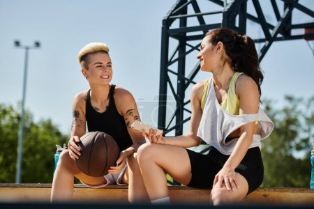 Zwei junge Frauen, athletisch und voller Elan, genießen einen sonnigen Tag im Freien, während sie mit einem Basketball auf dem Boden sitzen.