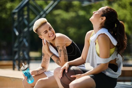 Téléchargez les photos : Deux jeunes femmes assises ensemble après avoir joué au basket à l'extérieur, profitant d'un moment d'amitié et de camaraderie. - en image libre de droit