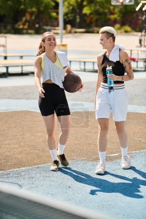 Foto de Dos mujeres jóvenes goteando un baloncesto al aire libre, mostrando su atletismo y trabajo en equipo en un día soleado de verano. - Imagen libre de derechos