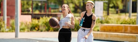 Two young athletic women, friends, are standing next to each other on the basketball court, enjoying a summer day of playing sports.