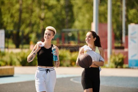 Deux jeunes femmes athlétiques se tiennent en confiance sur un terrain de basket par une journée ensoleillée, incarnant la force et l'amitié.