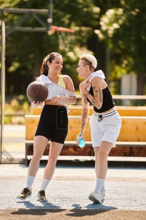 Two athletic young women dribbling and shooting hoops on a sunny outdoor basketball court in summer.