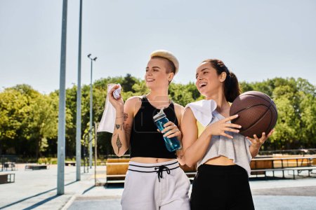 Dos amigas atléticas de pie juntas, sosteniendo pelotas de baloncesto en un entorno al aire libre de verano.