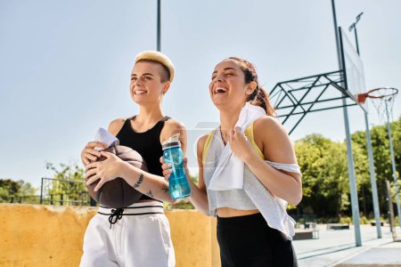 Téléchargez les photos : Deux jeunes femmes se tiennent ensemble à l'extérieur, prêtes à jouer au basket-ball sous le soleil d'été. - en image libre de droit