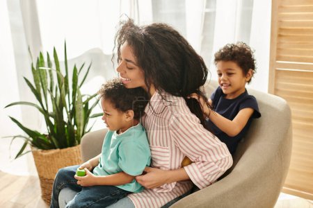 Téléchargez les photos : Petit garçon afro-américain mignon tressant les cheveux de sa mère joyeuse alors qu'elle tient son frère - en image libre de droit
