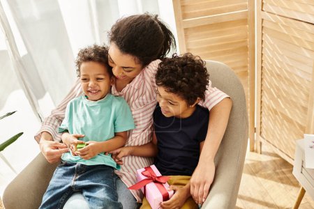 fröhliche afrikanisch-amerikanische dreiköpfige Familie, die Zeit miteinander verbringt, Gegenwart in Händen, Muttertag