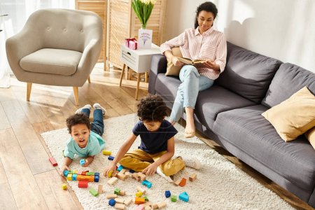 lustige afrikanisch-amerikanische Mutter sieht ihre Kinder beim Lesen von Büchern mit Spielzeug spielen