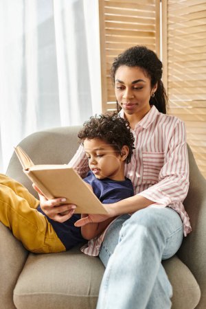 joyful beautiful african american mother reading interesting book with her adorable jolly son