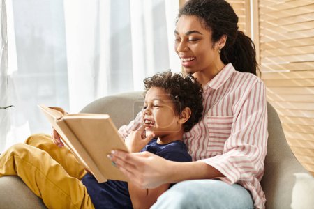 freudig schöne afrikanisch-amerikanische Frau liest interessantes Buch mit ihrem kleinen entzückenden Sohn