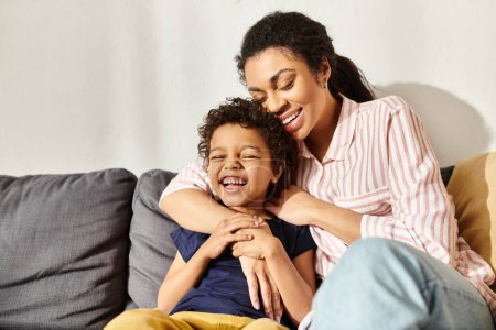 fröhlich liebende afrikanisch-amerikanische Mutter umarmt ihren entzückend lächelnden Sohn im Wohnzimmer