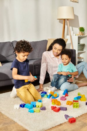 jolly beautiful african american mother watching her adorable little sons playing with toys at home