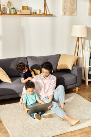 fröhliche afrikanisch-amerikanische Mutter hat Spaß mit ihren kleinen Söhnen vor dem Laptop zu Hause