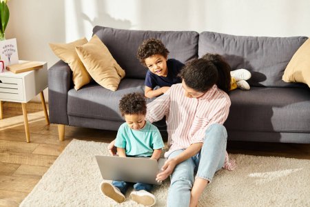 Téléchargez les photos : Joyeuse mère afro-américaine en tenue de maison regardant des films avec ses adorables petits fils à la maison - en image libre de droit