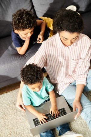 Téléchargez les photos : Vue du dessus de belle femme afro-américaine regardant des films sur ordinateur portable avec ses deux adorables fils - en image libre de droit