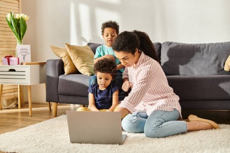 Konzentrierte afrikanisch-amerikanische Mutter und Sohn schauen auf Laptop mit anderen entzückenden Jungen auf dem Hintergrund
