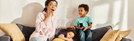 femme afro-américaine choquée en vêtements de maison regarder des films avec ses adorables fils, bannière