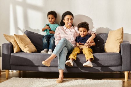 fröhliche afrikanisch-amerikanische Mutter in kuscheliger Kleidung beim Kinobesuch mit ihren entzückenden kleinen Söhnen