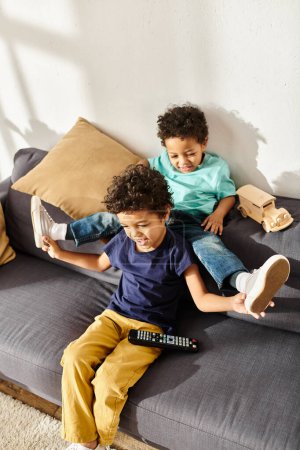 joyful adorable brothers in homewear having fun while sitting in front of TV in living room