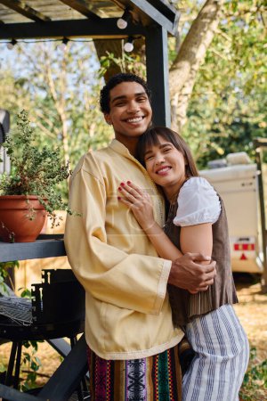 An interracial couple hugs tenderly in front of a lush potted plant, symbolizing their deep connection amidst a natural setting.