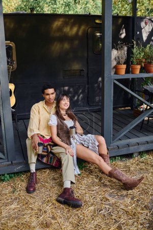 Téléchargez les photos : Un couple interracial assis à proximité, profitant d'un moment romantique dans un camping-car entouré par la beauté de la nature. - en image libre de droit