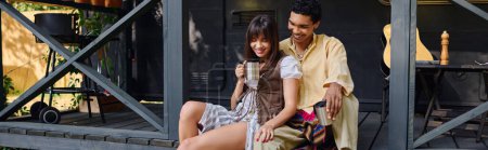 Téléchargez les photos : Un homme et une femme se tiennent ensemble sur un porche, profitant de la vue sereine autour d'eux. - en image libre de droit