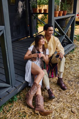 A man and a woman of different races relax together on a wooden porch, enjoying each others company in a peaceful setting.