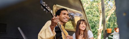 Ein Mann spielt leidenschaftlich seine Gitarre, während eine Frau neben ihm steht und die Musik in einer landschaftlich reizvollen Naturkulisse genießt..