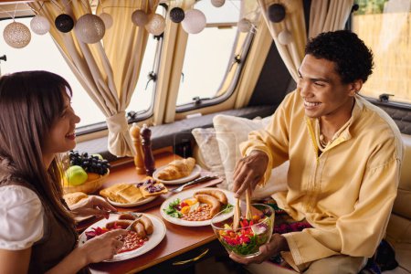 Una pareja interracial se sienta en una mesa en una caravana, disfrutando de un almuerzo romántico juntos.