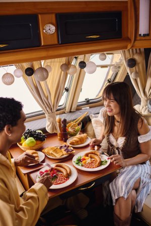 Una pareja interracial disfrutando de una deliciosa comida juntos en una mesa en una caravana durante una escapada romántica.