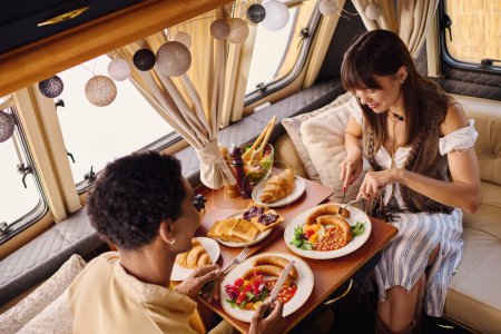 couple enjoying a cozy lunch inside a camper van, plates of delicious food in front of them.