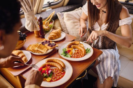 A woman sits at a table, enjoying a variety of delicious dishes spread out in front of her during a romantic getaway in a camper van.