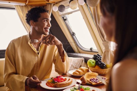 Foto de Una pareja interracial disfrutando de un delicioso almuerzo dentro de una caravana, creando un ambiente romántico. - Imagen libre de derechos