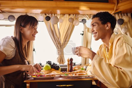 Photo for An interracial couple enjoying a romantic lunch together in a camper van on a cozy getaway. - Royalty Free Image