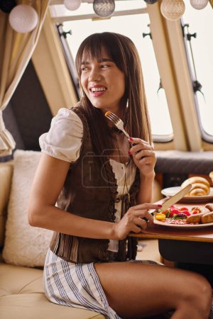 A woman sitting peacefully on a couch, holding a plate of appetizing food.