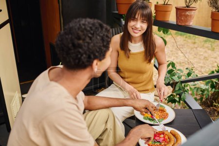 Téléchargez les photos : Un couple interracial dégustant un délicieux repas ensemble tout en étant assis sur un porche. - en image libre de droit