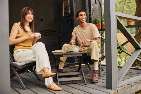 Una pareja interracial se relaja juntos en un acogedor porche, disfrutando de la compañía de los demás en un entorno tranquilo.